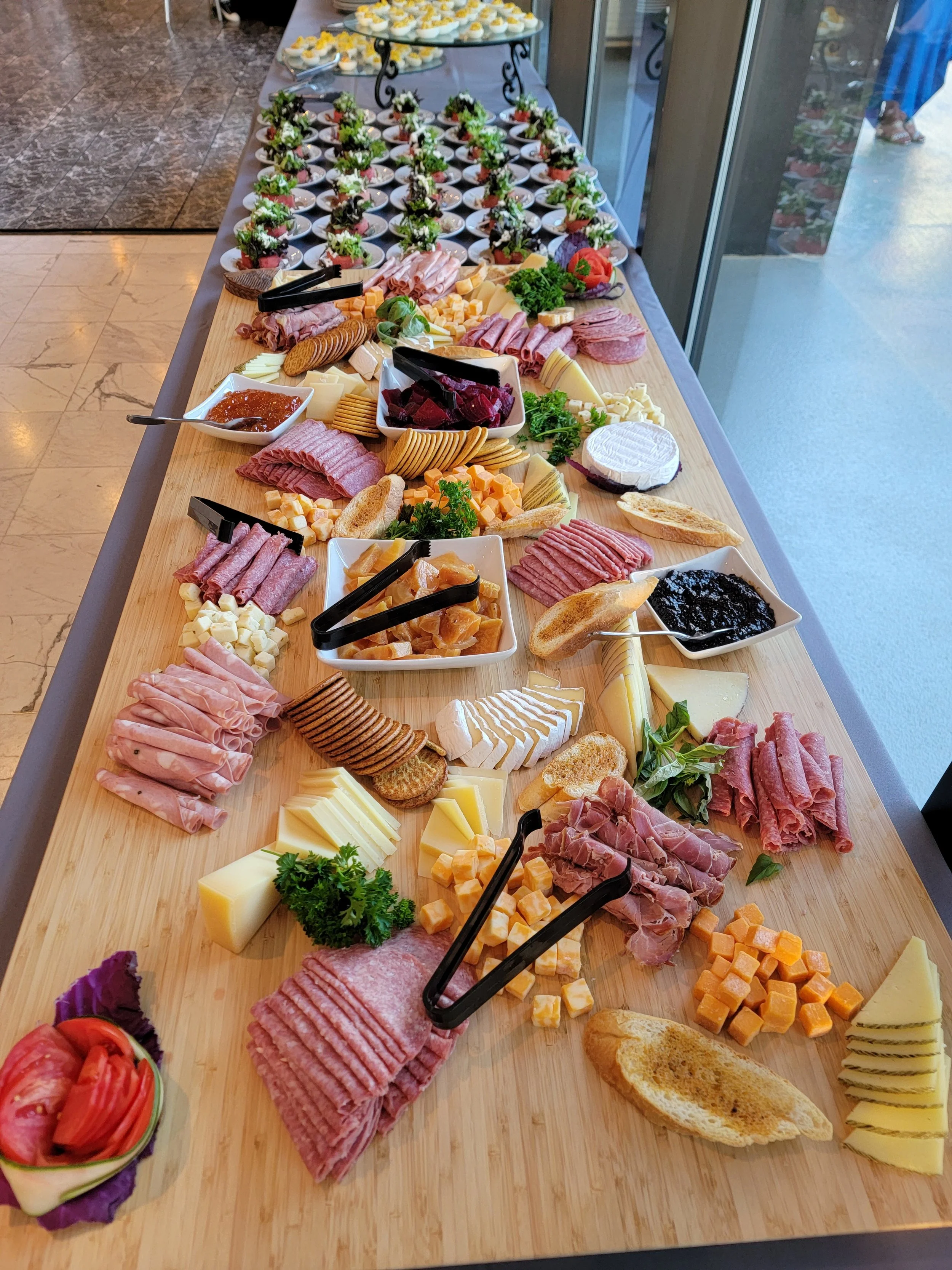 A curated charcuterie table with an assortment of cheeses, cured meats, crackers, fruit, and vegetable garnishes, arranged on a wooden surface by luxury in-house catering at JPS Events at Regions Tower in Downtown Indianapolis.