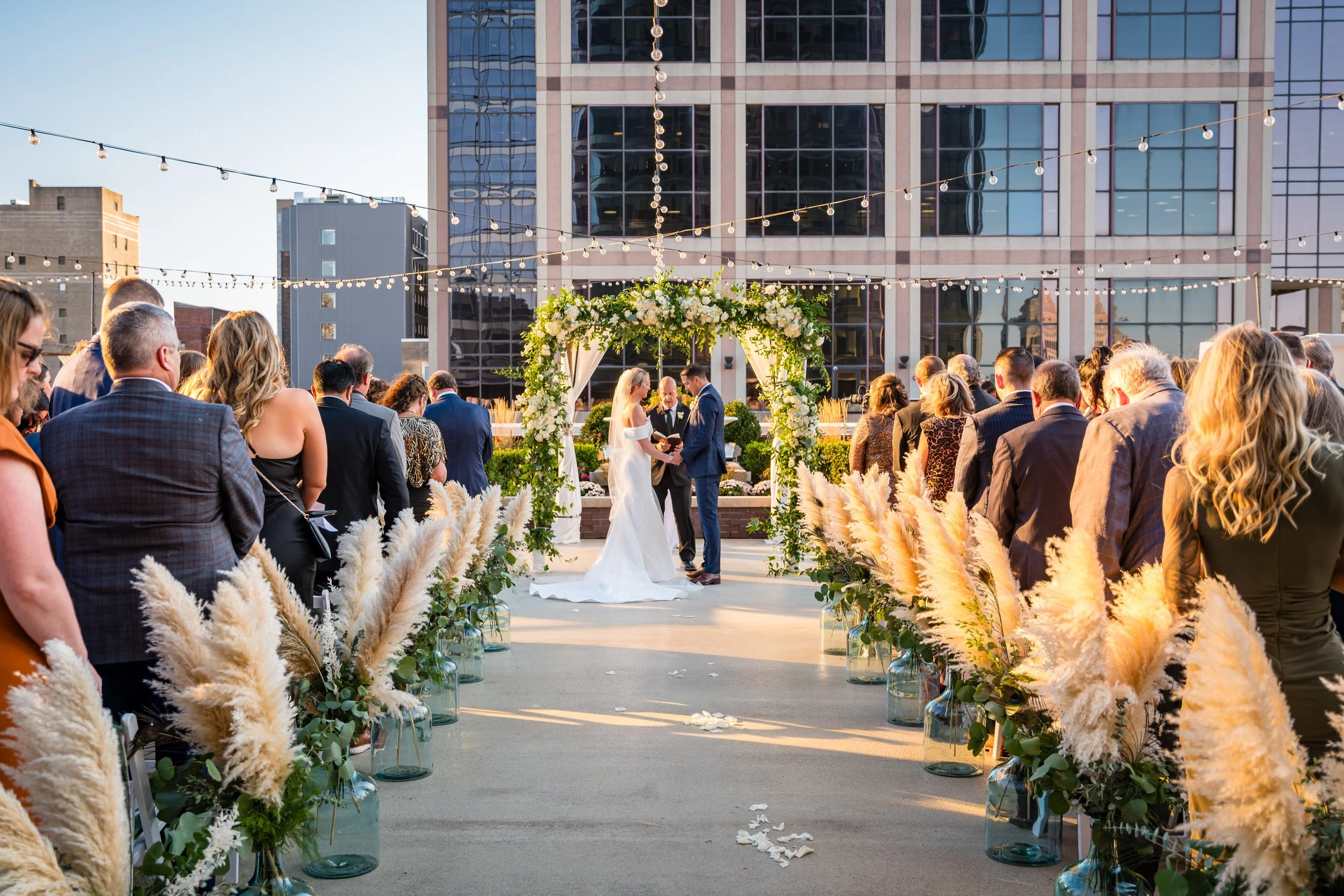 Sunset wedding ceremony on the 11,000 sq ft 5th-floor penthouse terrace at JPS Events at Regions Tower, featuring custom pampas grass aisle styling, 360 skyline views, and all-inclusive coordination in downtown Indy.