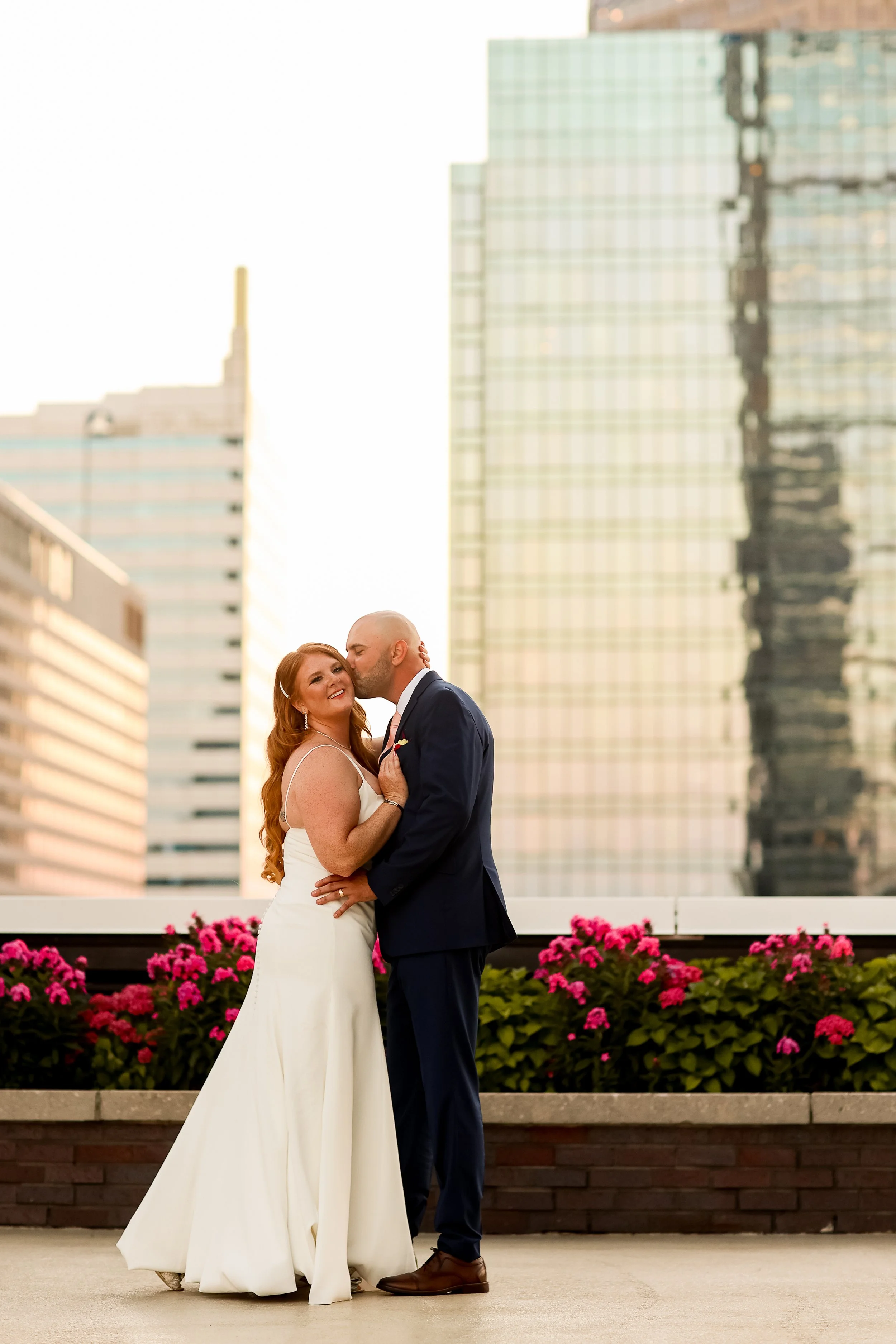 A bride and groom sharing a kiss on the exclusive 5th-floor rooftop terrace at JPS Events at Regions Tower in Downtown Indianapolis, framed by custom in-house flowers and 360-degree skyline views.