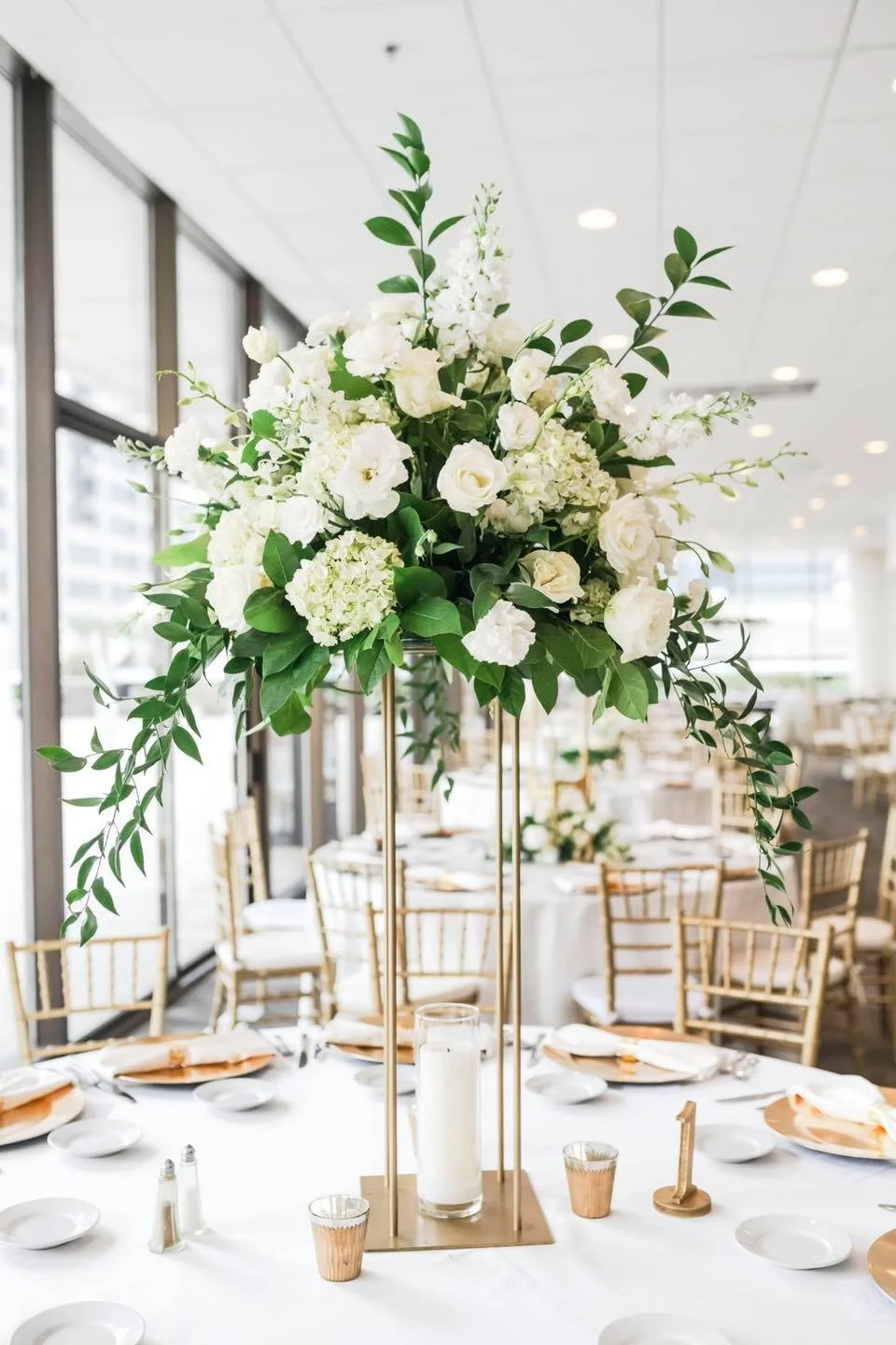 Elegant floral centerpiece with white flowers and green foliage on a dining table at a formal event.