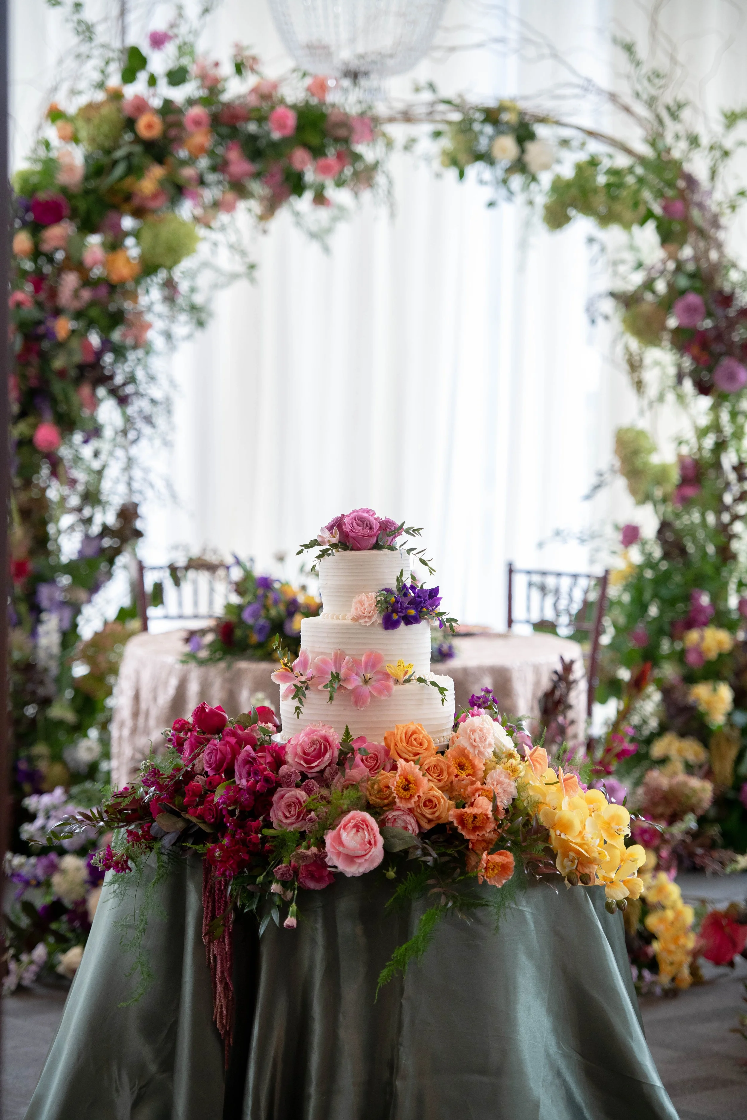 Custom 3-tiered wedding cake display framed by over-the-top floral arrangements designed by the in-house florists at JPS Events at Regions Tower. Offers custom floral design at wholesale pricing in downtown Indianapolis.