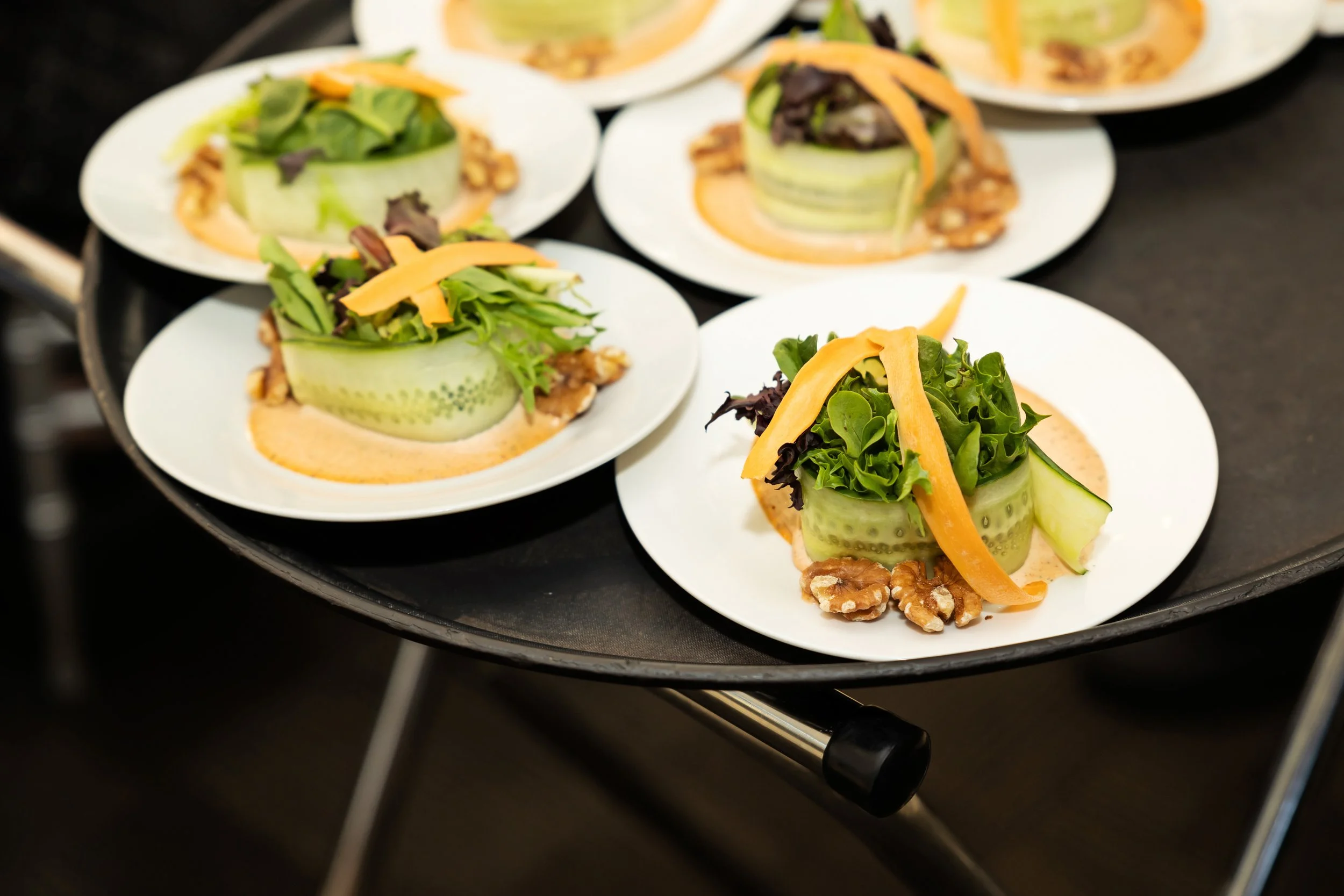 Several plates of a unique cucumber wrapped salad bowl filled with mixed greens and shredded cheese, garnished with nuts, on a black tray—one of our unique salad options by luxury in-house catering at JPS Events at Regions Tower in Downtown Indy.  