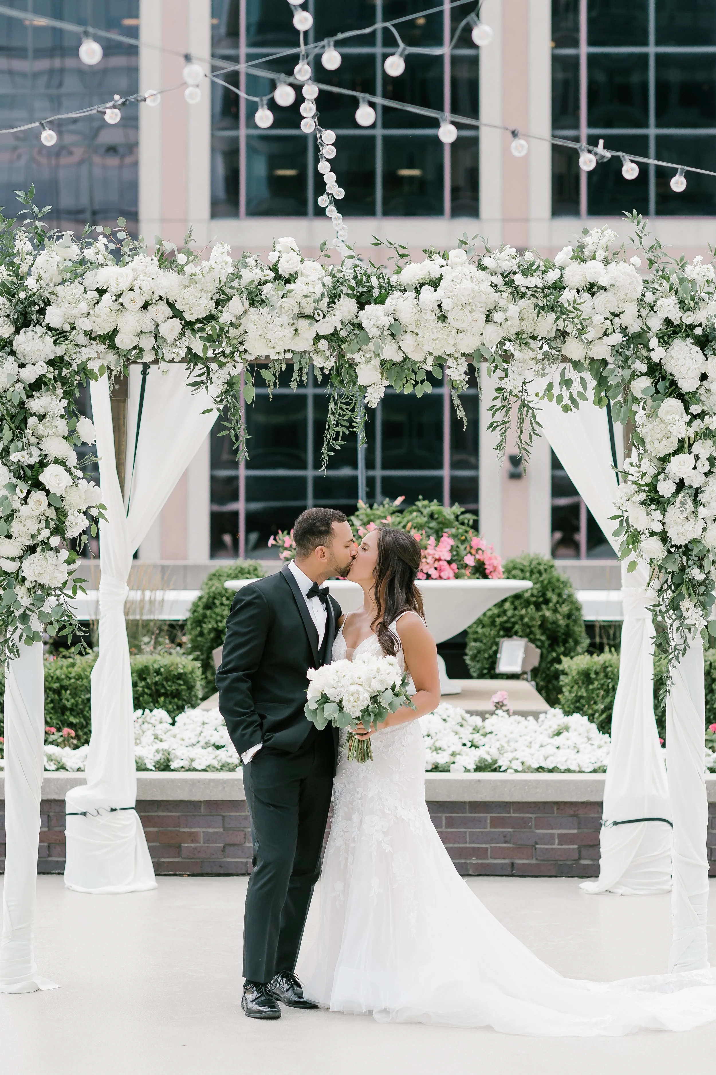 Outdoor rooftop ceremony on the 5th-floor terrace at JPS Events at Regions Tower, featuring ambient string lighting, in-house custom floral arch at wholesale pricing, & seamless indoor backup transition in downtown Indy.