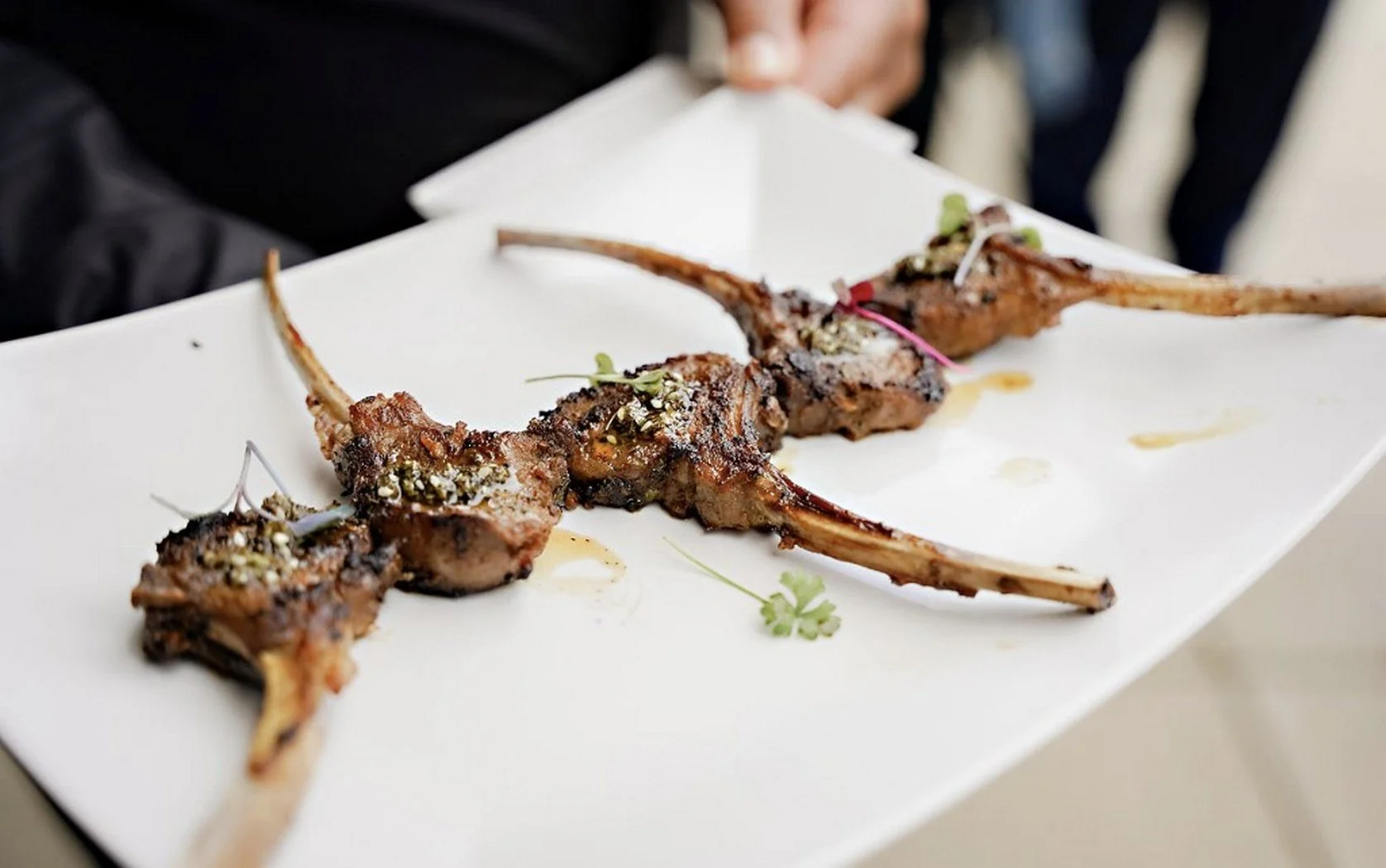 Grilled lamb chops garnished with herbs on a white rectangular plate by the chef-driven in-house catering team at JPS Events at Regions Tower, an all-inclusive luxury wedding venue in Downtown Indianapolis.