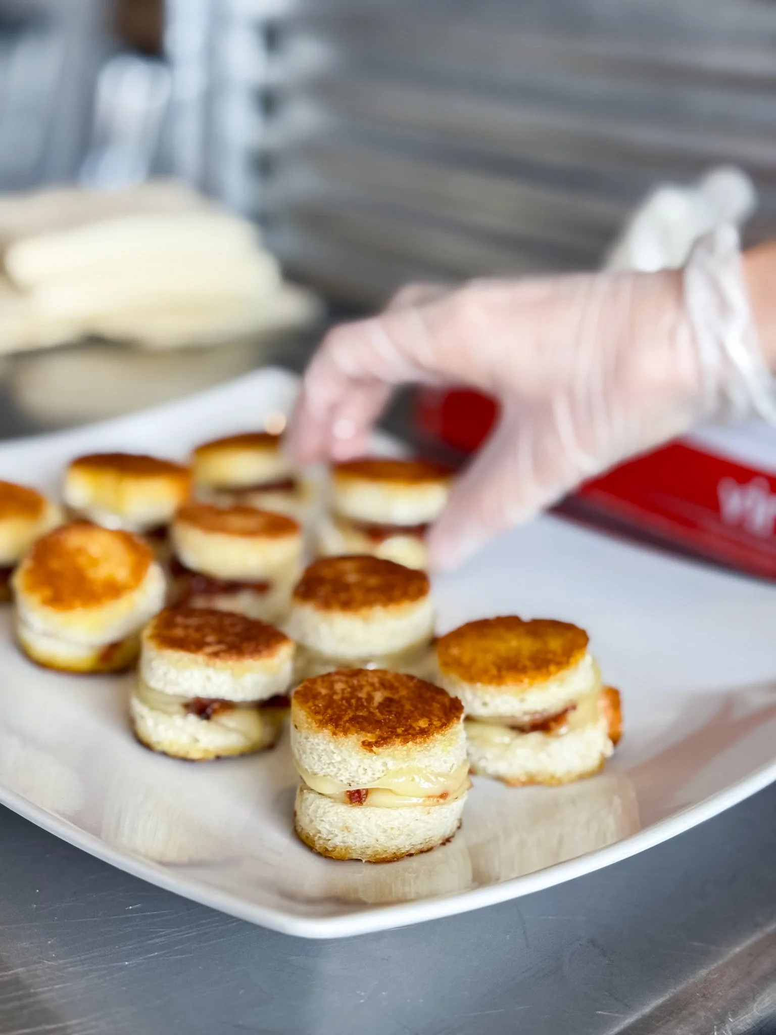 Close-up of bite-sized appetizers with layered ingredients, including a creamy filling and a crispy top, arranged on a white rectangular plate.