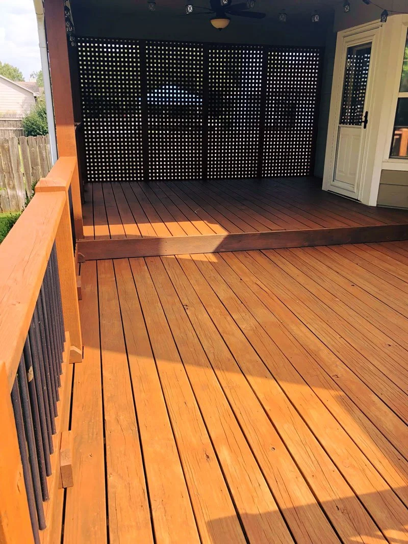 Wooden deck with railing, screened privacy partition, and door leading into house