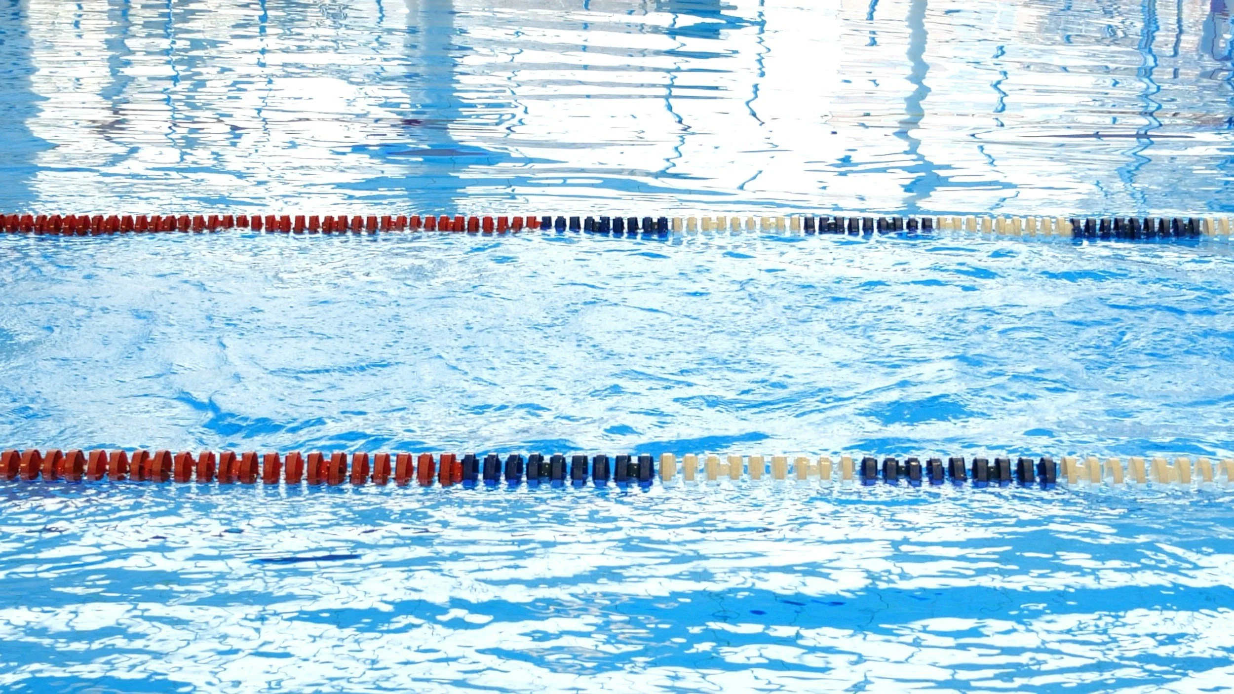 Swimming pool with lane dividers and reflections of overhead lights on the water surface.