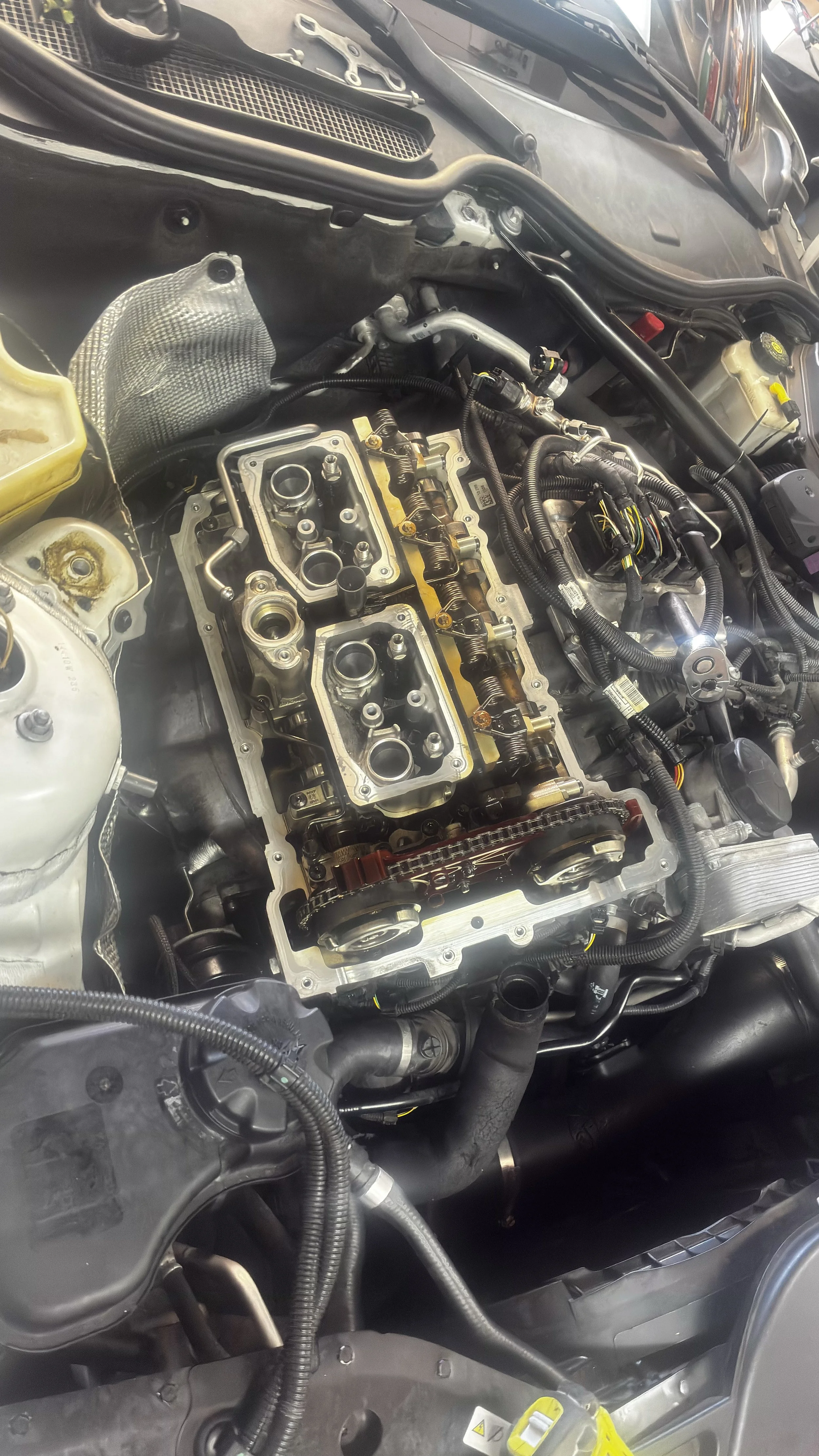View of a car engine with the valve cover removed, exposing the camshafts, timing chain, and other internal components.