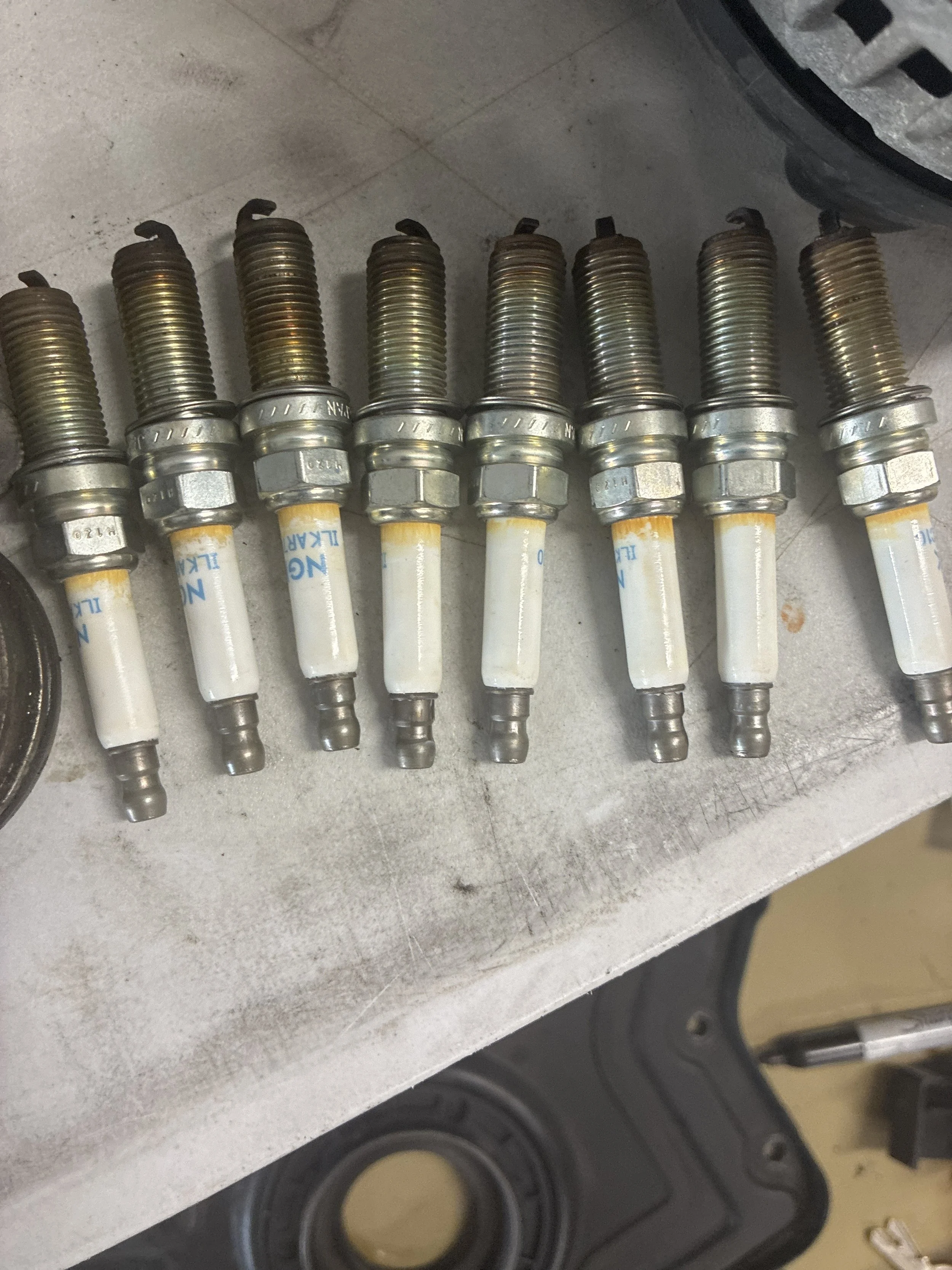 Eight used spark plugs lined up on a grey work surface.