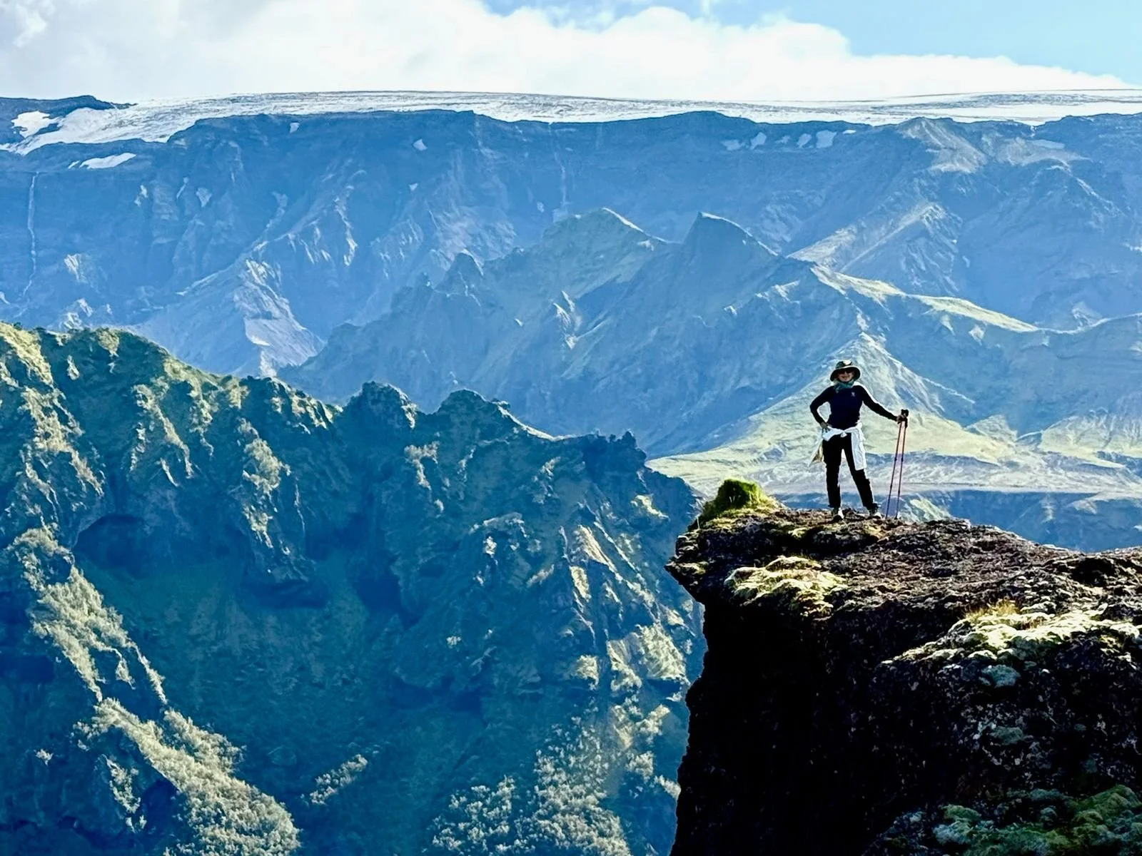 Woman in hiking gear and poles on top of mountain edge with background showcasing Hvannárgil valley