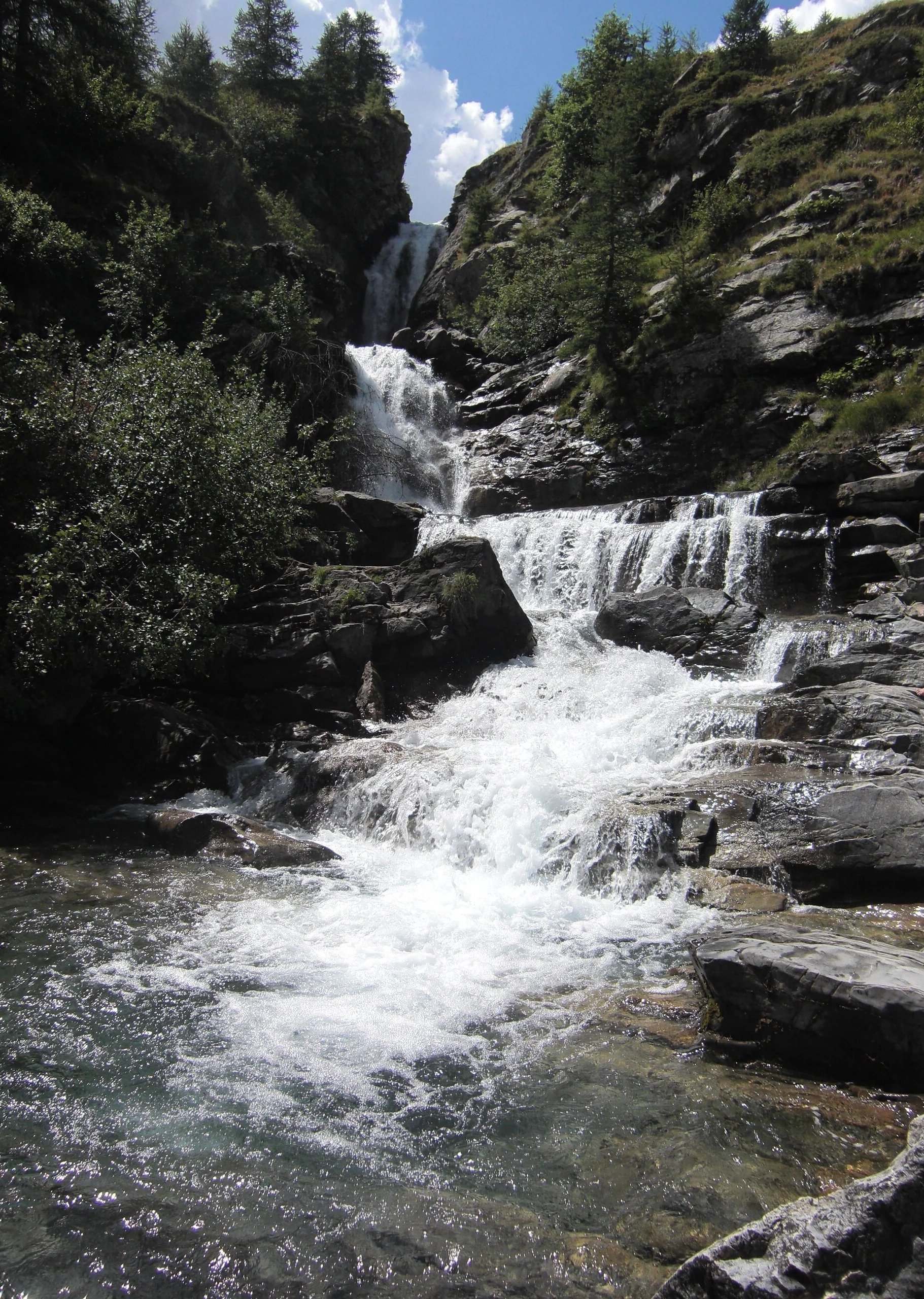 Cascade of spring water cutting through mountain rocks and trees either side