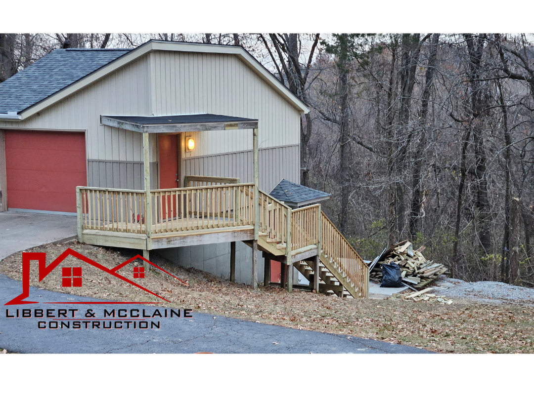 New wooden deck with stairs attached to the back of a house, surrounded by trees and construction materials, with a logo for Libbert & McLaine Construction in the bottom left corner.