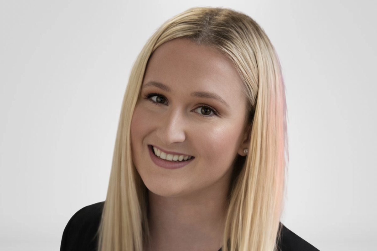 Portrait of a young woman with long blonde hair smiling at the camera against a plain background.
