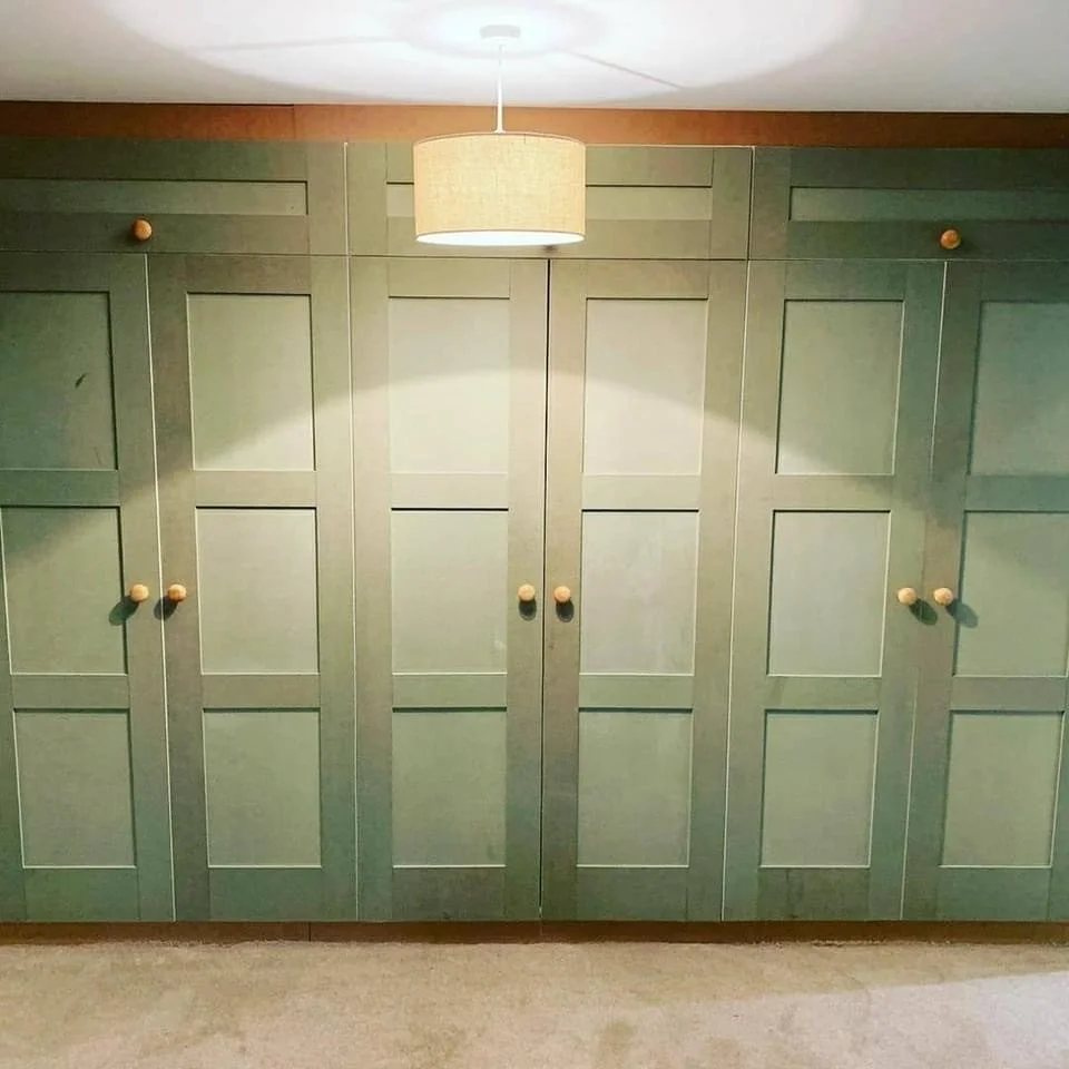Green built-in closet with double doors and wooden knobs, illuminated by a ceiling-mounted beige lampshade.