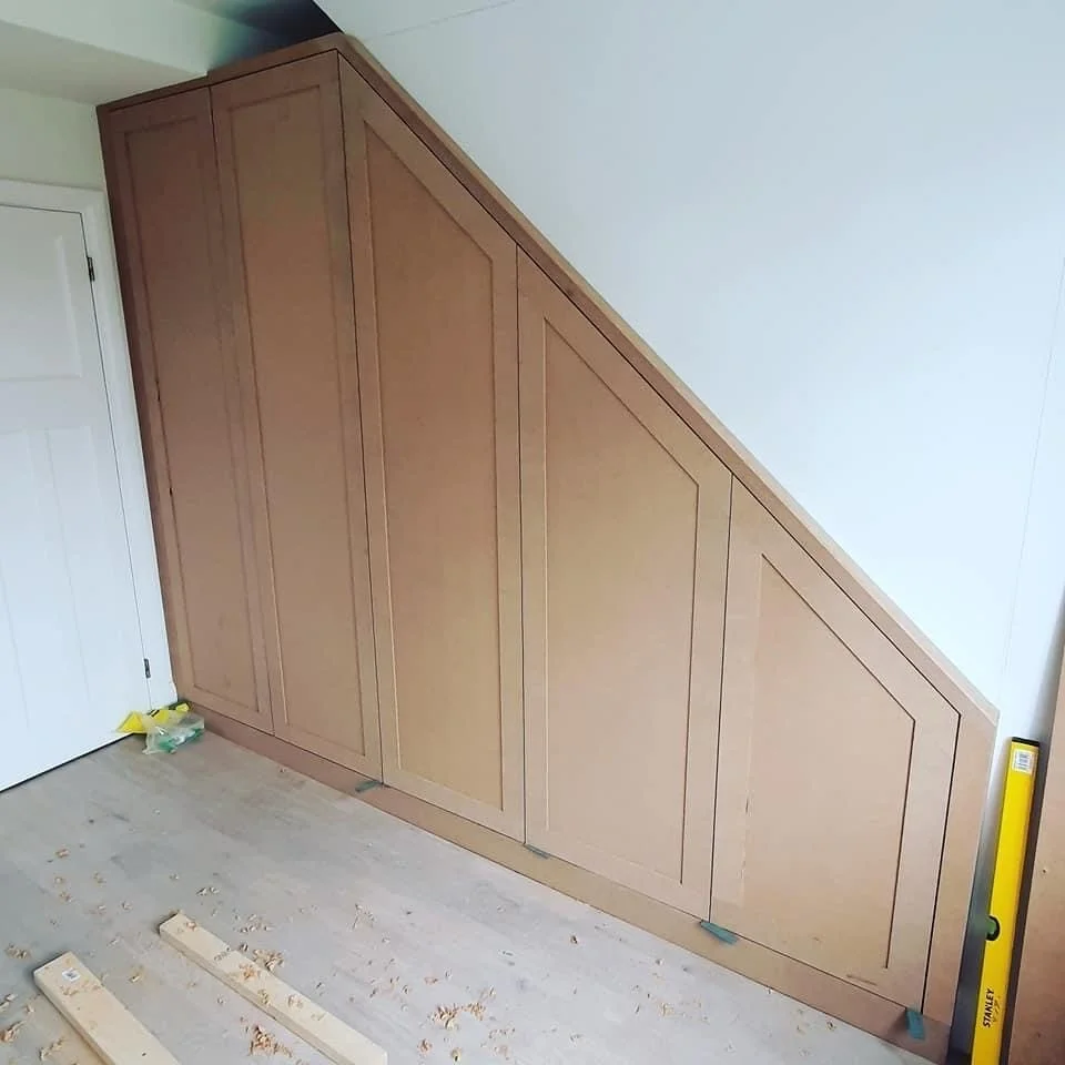 Wooden cabinet or wall paneling with geometric designs, installed on a wall under a sloped ceiling in a room.
