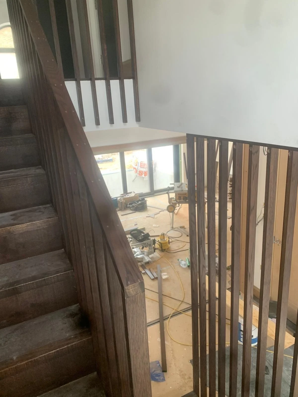 Interior view of a house under construction, showing wooden stairs, a railing, and construction tools on the floor.