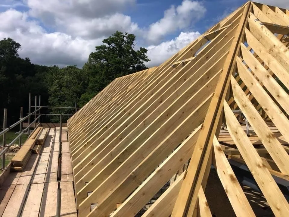 Wooden roof framing under construction on a building, with a clear sky and trees in the background.
