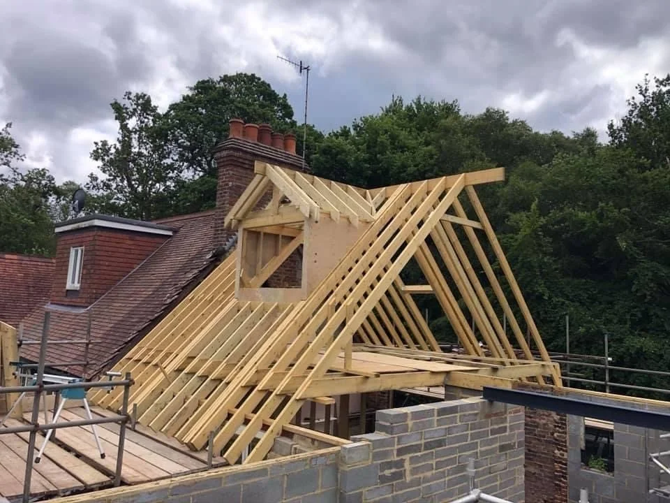 Wooden framework for a roof extension on top of a brick house under construction.