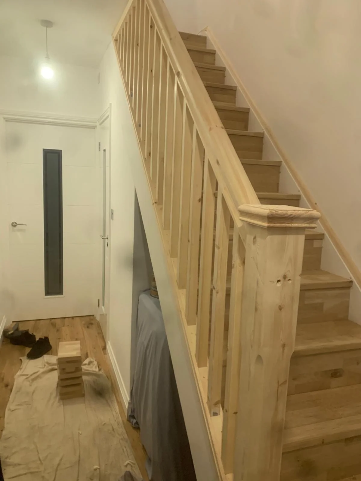 Wooden staircase with railing in an interior space, with construction tools and materials visible on the floor.