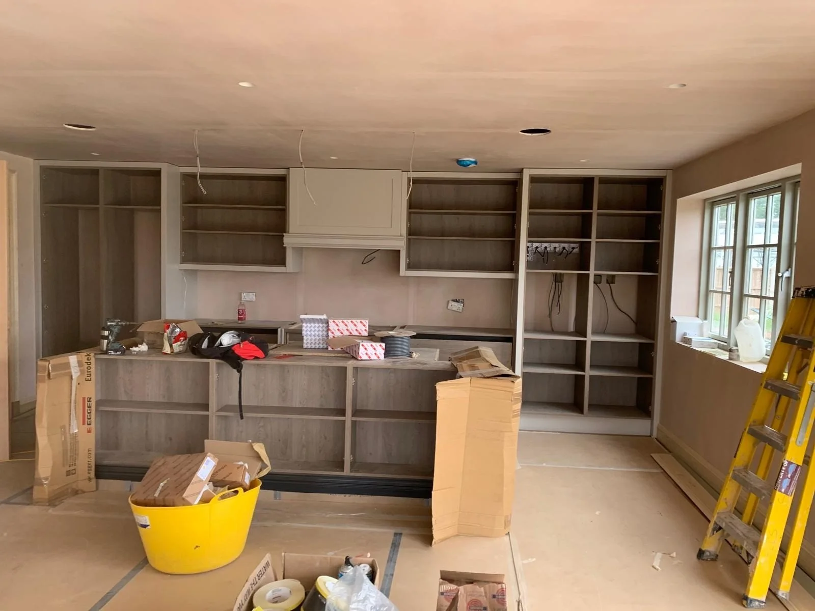 Kitchen under construction with empty cabinets, construction tools, and supplies scattered around.
