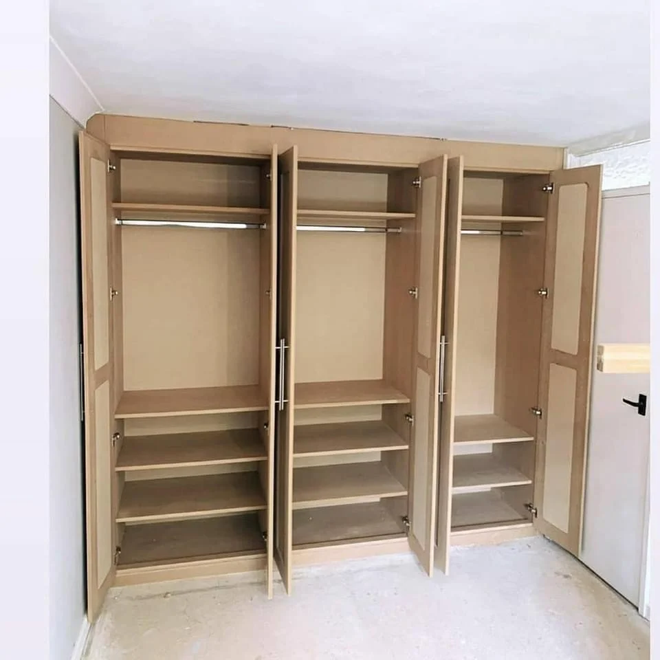 Empty wooden closet with three sections, each having shelves and a hanging rod, in a room with light-colored walls and carpeted floor.