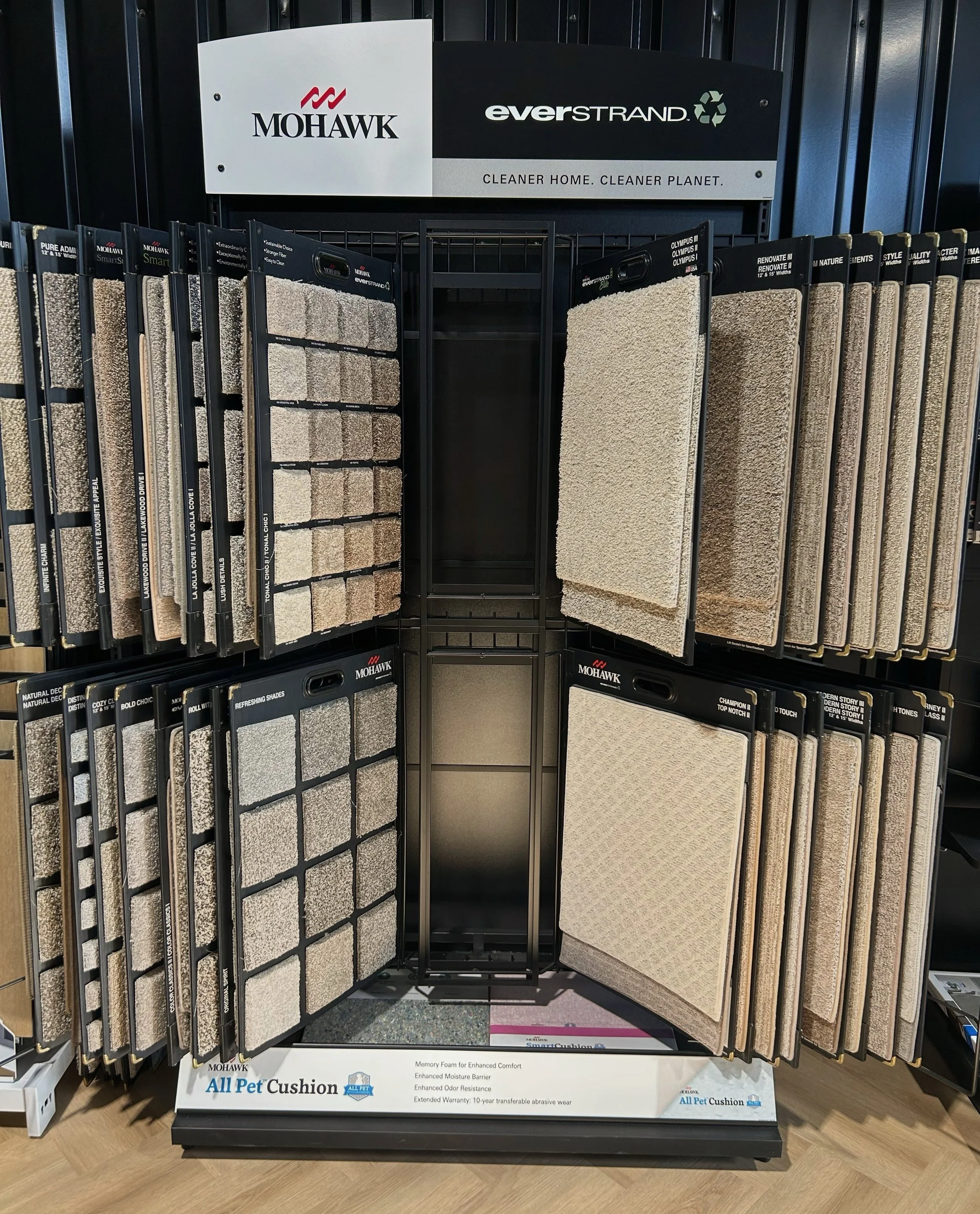 Display of various carpet samples in a store, arranged on black racks with a sign above reading "Mohawk" and "EverStrand."