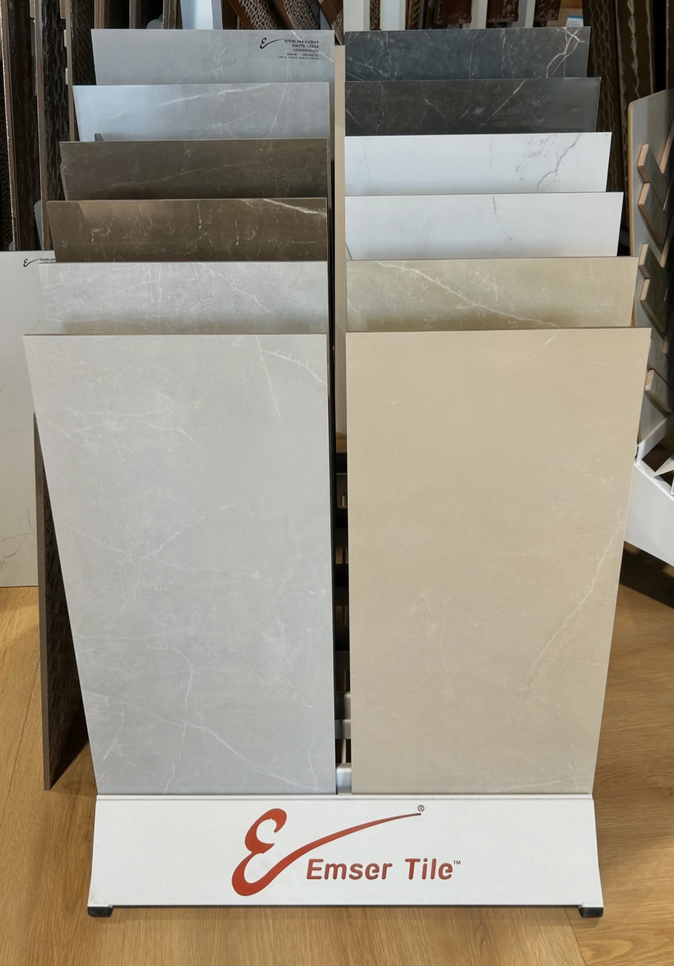 Display stand with various marble-look tile samples in shades of gray, beige, and white at a store called Emser Tile.