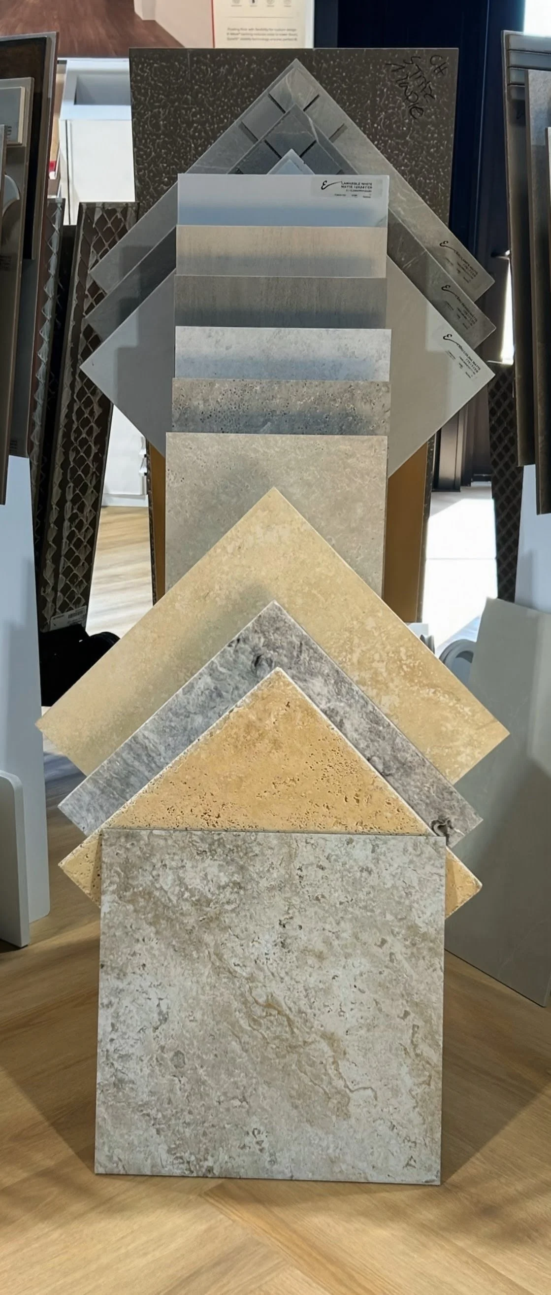 Sheet samples of various neutral-colored flooring and tile materials displayed in a retail store.