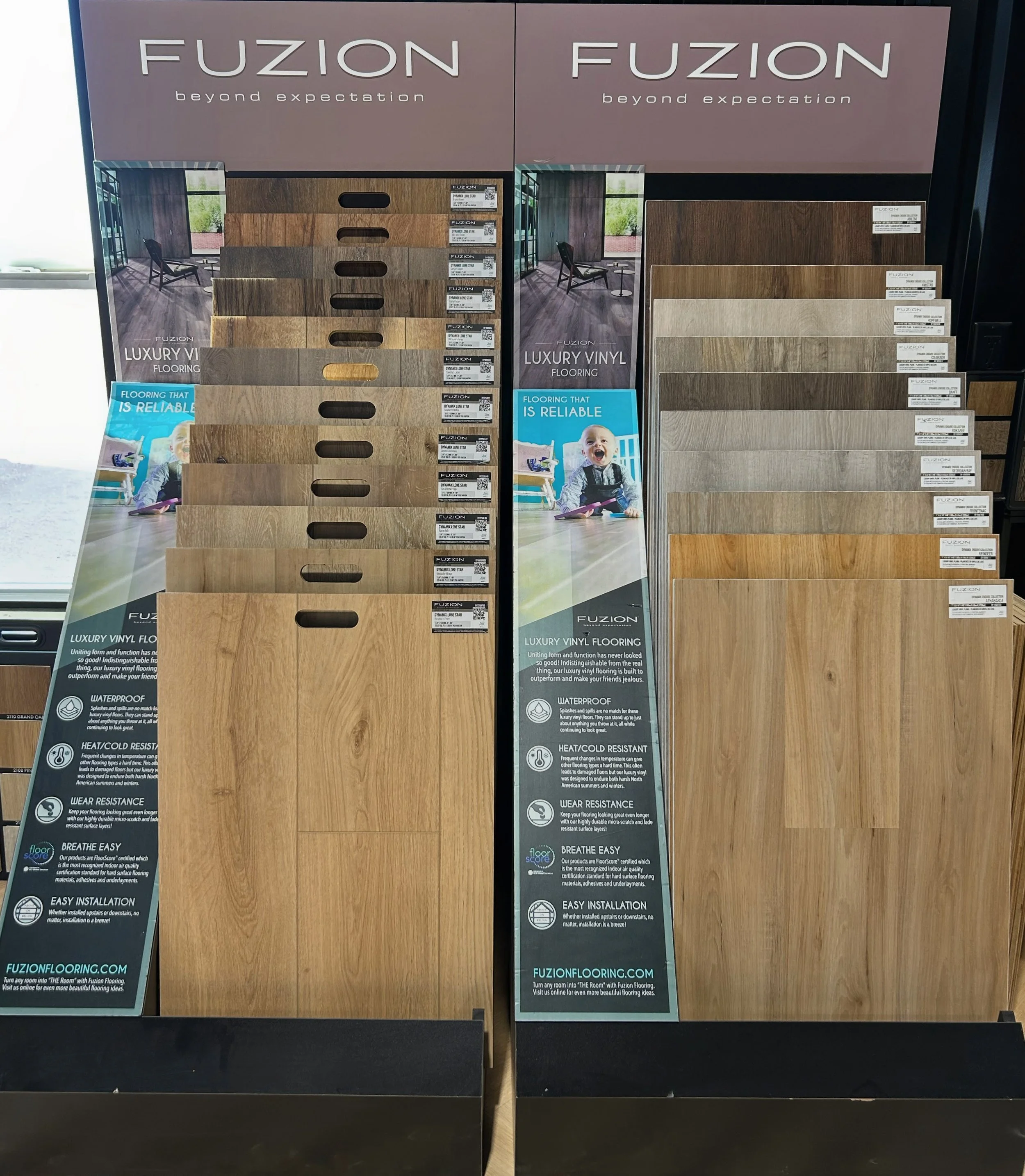 Display of luxury vinyl flooring samples in various wood tones arranged on shelves at a flooring store, with branding and informational signage.