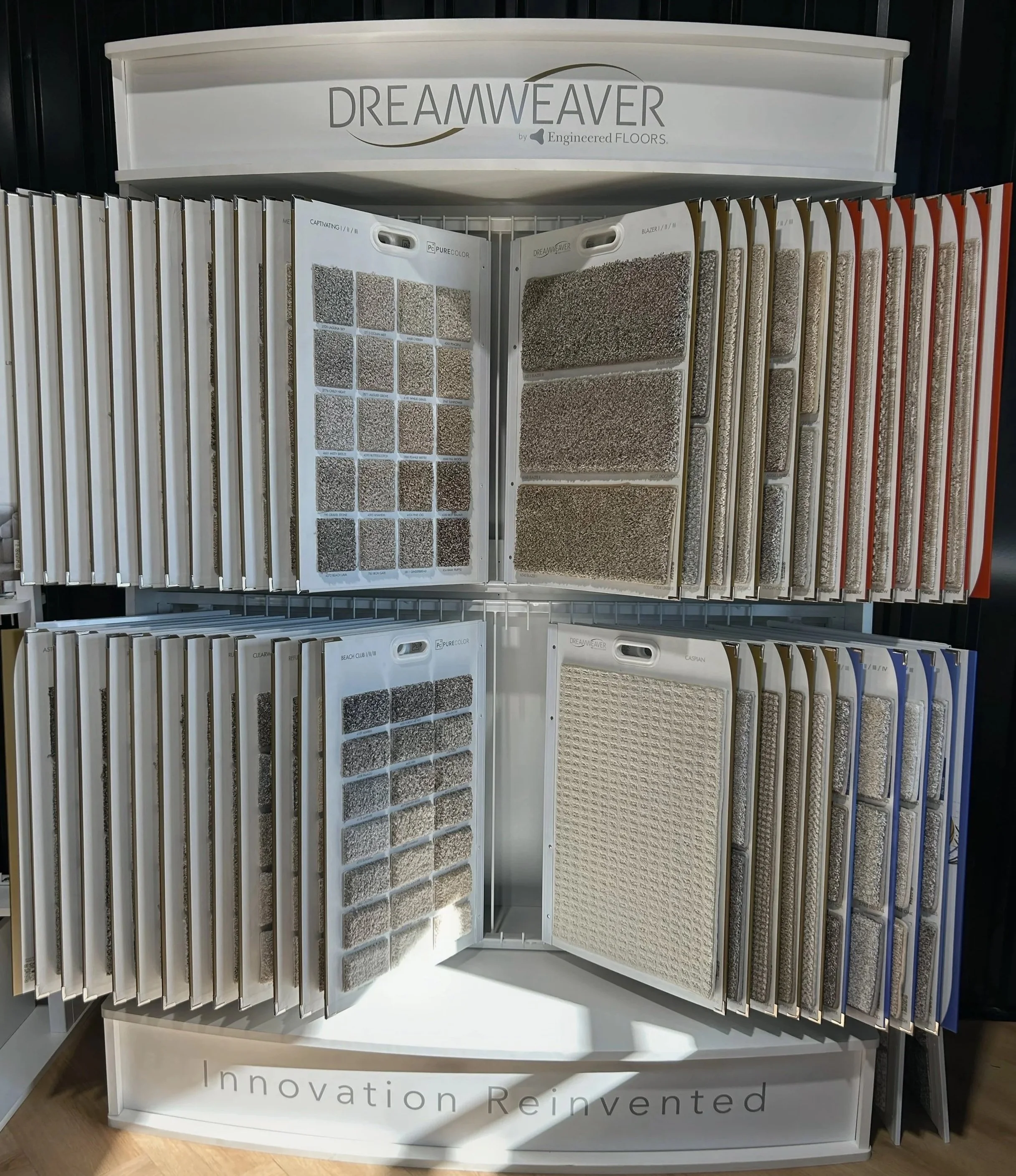 Display of carpet samples arranged on a white stand with the brand name Dreamweaver and slogan 'Innovation Reinvented' at the bottom. The samples show various colors and textures of carpets.