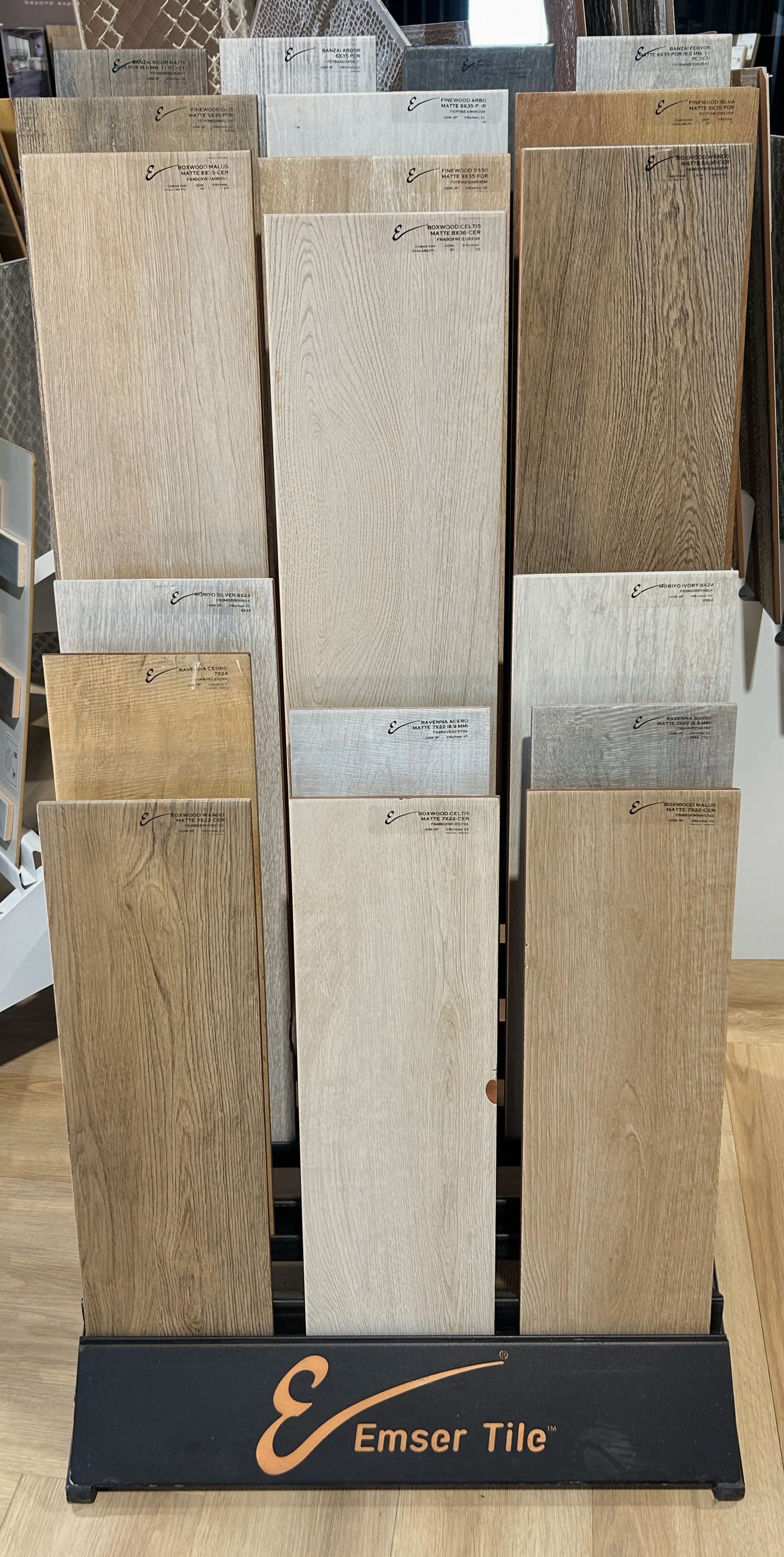 Display of various wood flooring samples, including oak and ash species, in different finishes such as matte and natural, at Emser Tile store.
