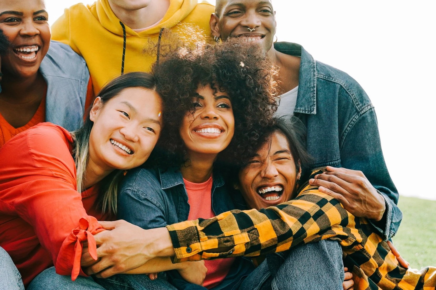 Group of six diverse friends smiling and hugging outdoors.