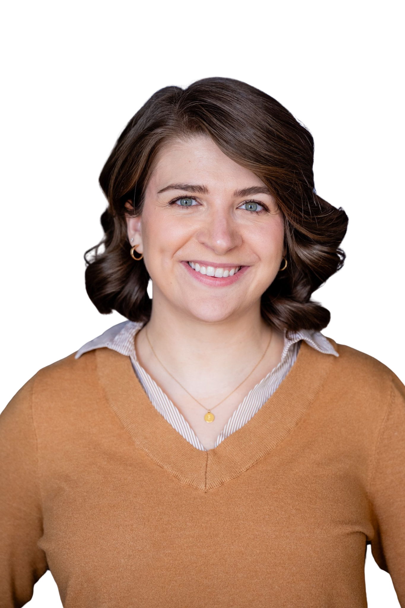 Close-up of a smiling woman with brown hair, blue eyes, gold hoop earrings, wearing a gold necklace, a white collared shirt, and a tan sweater.