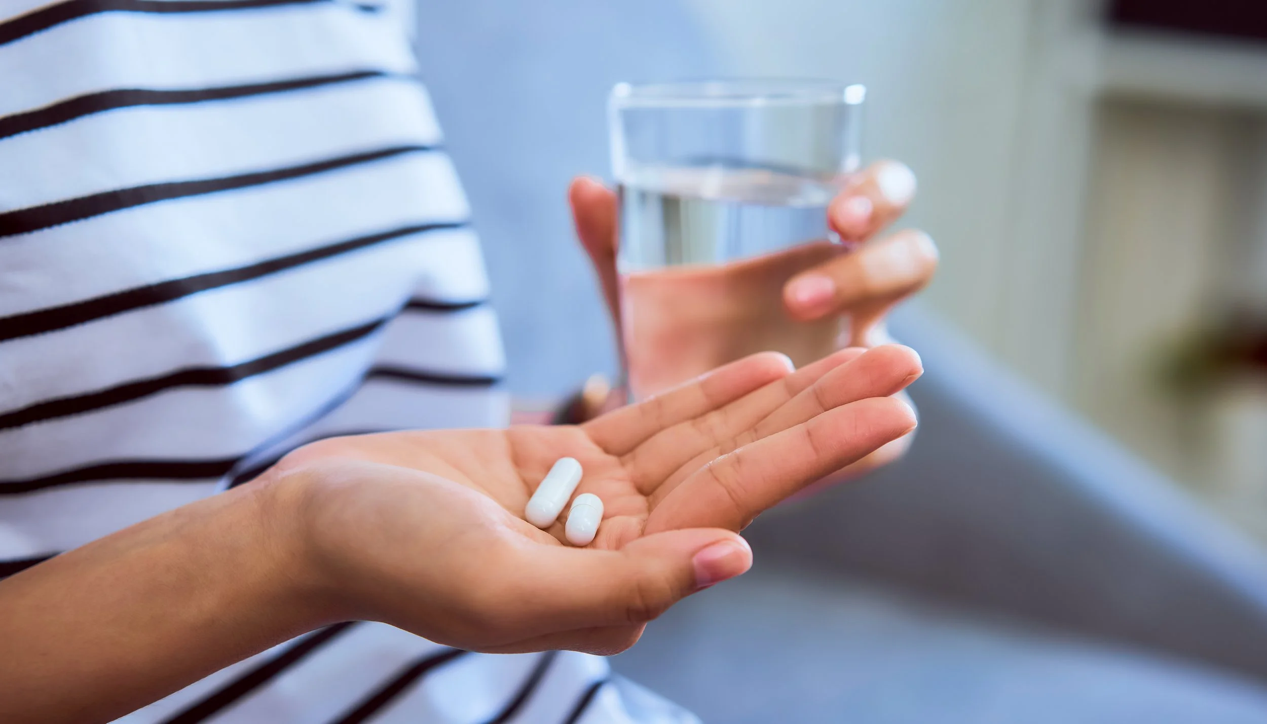 Person holding three white pills in their hand with a glass of water in the other hand.