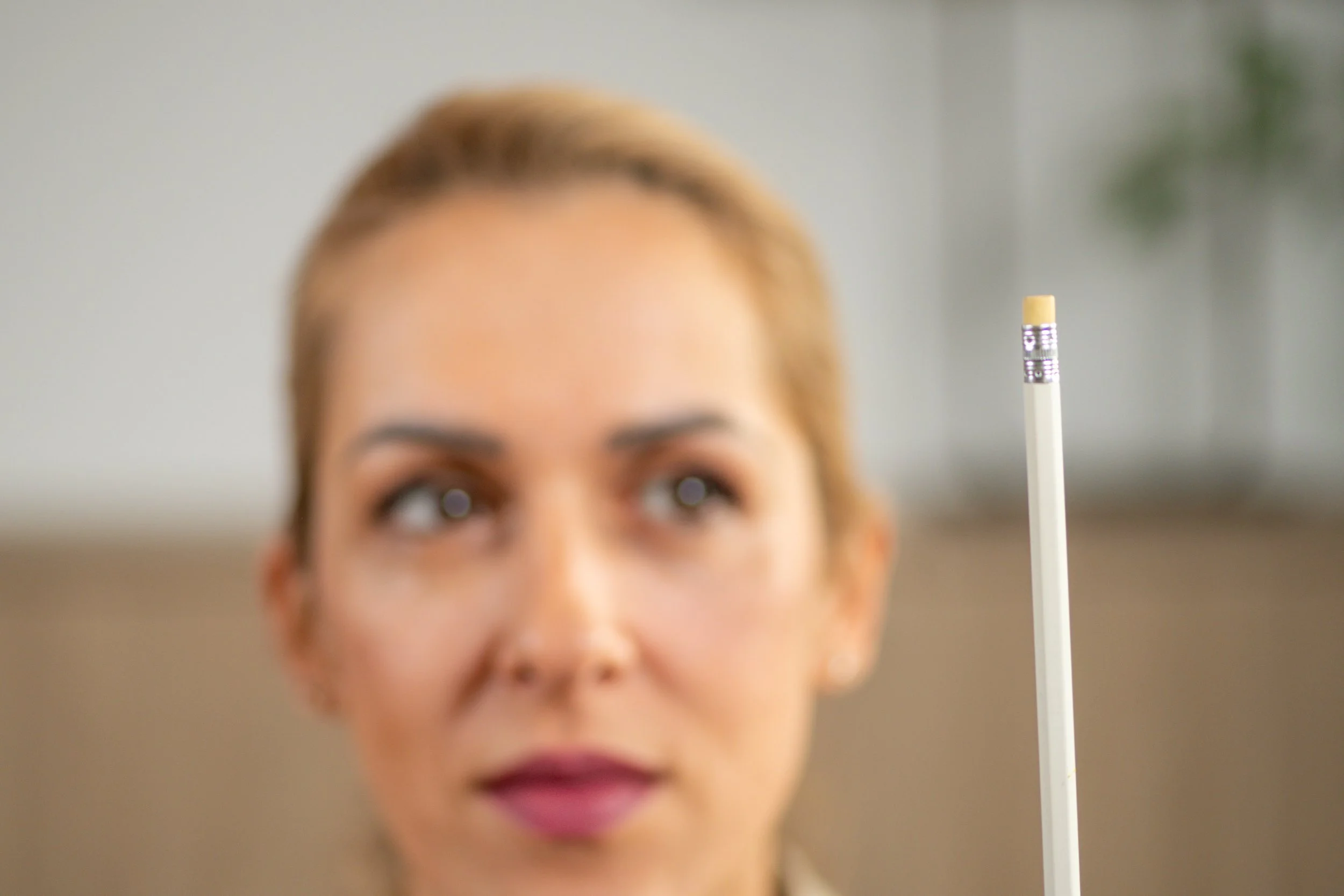A woman with blonde hair looking at a large white pencil with an eraser at the end.