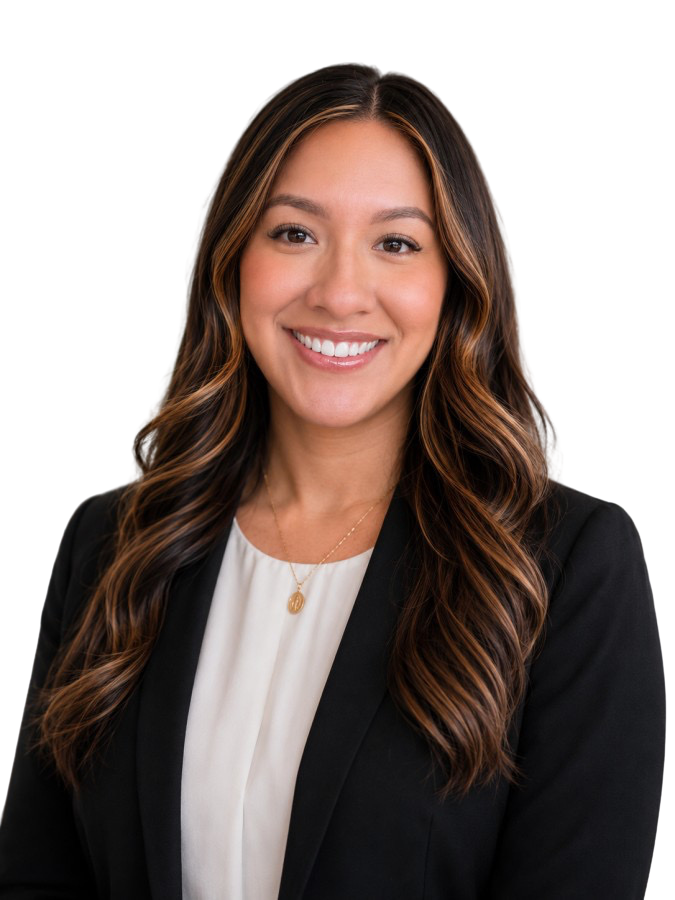 A woman with long, wavy brown hair, smiling, dressed in a black blazer and white blouse, wearing a gold necklace with a pendant.