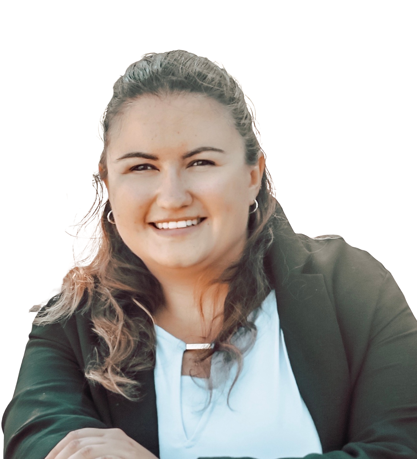 Smiling woman with long, wavy hair, wearing hoop earrings, a black jacket, and a white shirt, sitting outdoors against a white background.