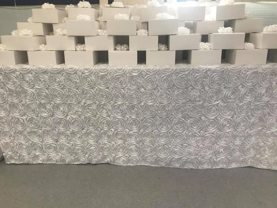 Table decorated with white roses and small white gift boxes on top.