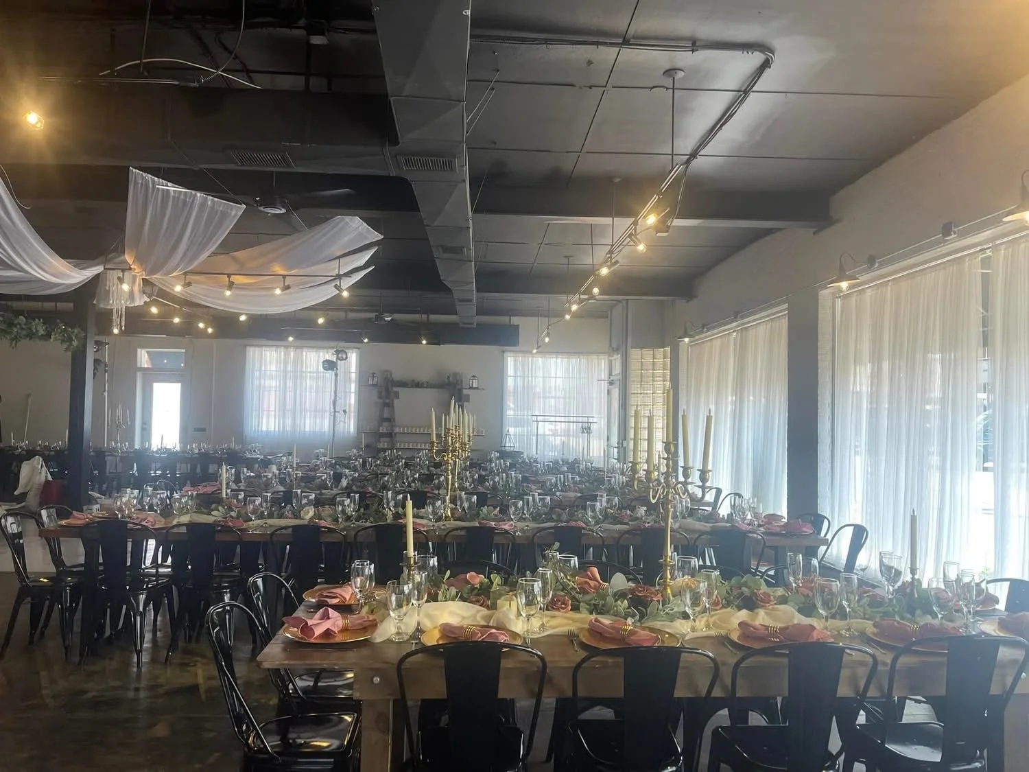 Event space decorated with elegant table settings, gold candelabras, and draped fabric on the ceiling, preparing for a formal celebration.