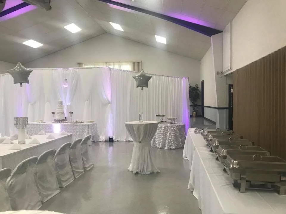 Event space decorated with white drapery, silver star balloons, a tiered cake, and tables set for a celebration.