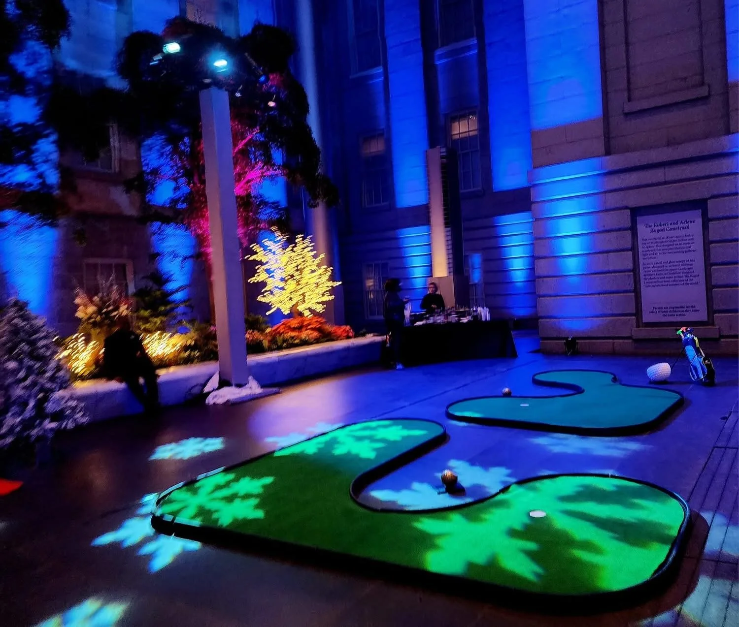 Indoor miniature golf course with two holes, illuminated with colorful lights, and a golf bag and golf balls near the right side.