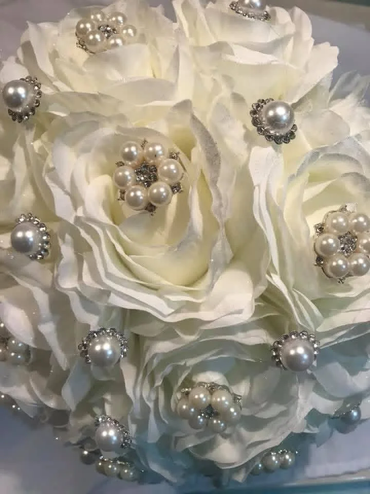 A bouquet of white artificial flowers decorated with pearl and rhinestone brooches.