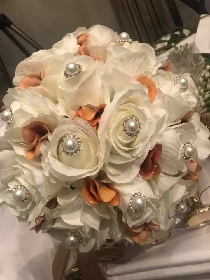A bouquet of white and peach flowers decorated with pearl brooches and rhinestones.