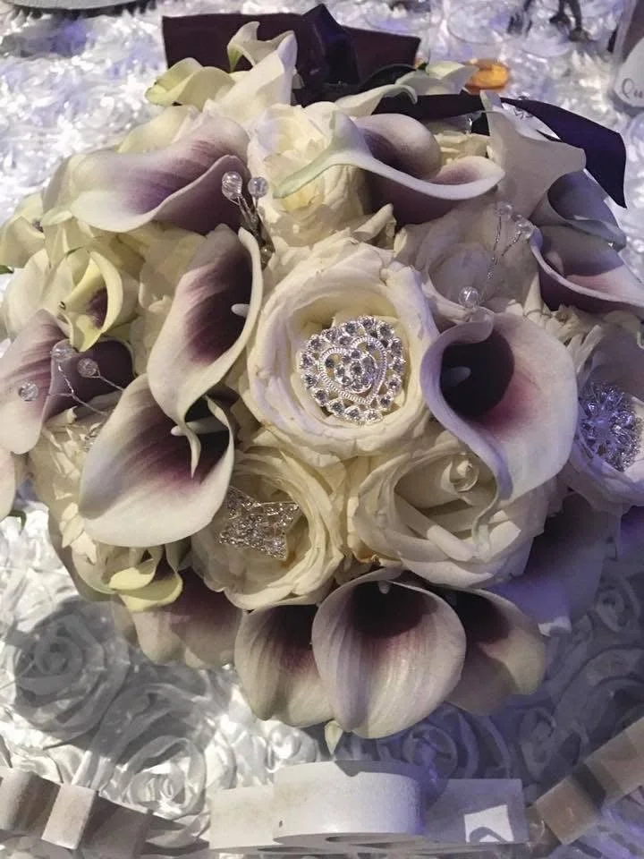 A wedding bouquet with white calla lilies and ivory roses, decorated with rhinestone jewelry and ribbons.
