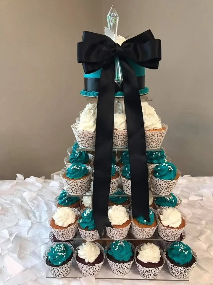 Cupcake tower decorated with teal and white frosting, topped with a black bow and a tall, clear crystal ornament.