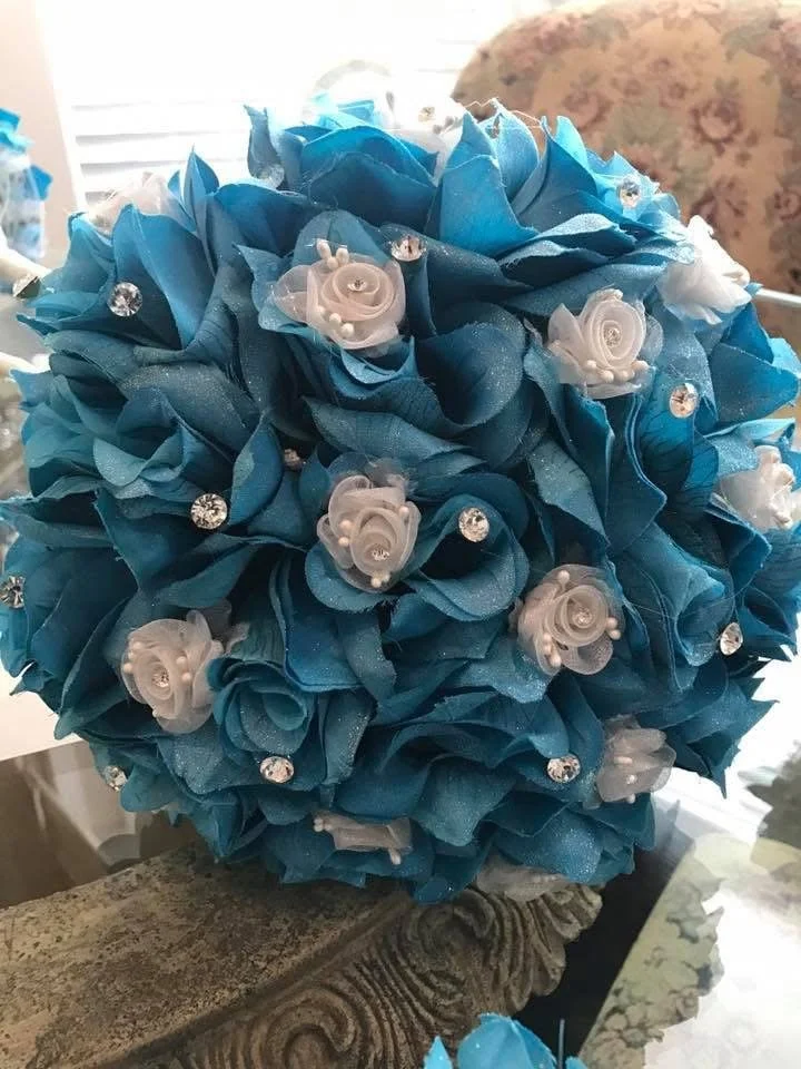 A bouquet of blue and white flowers with decorative white roses and rhinestones.
