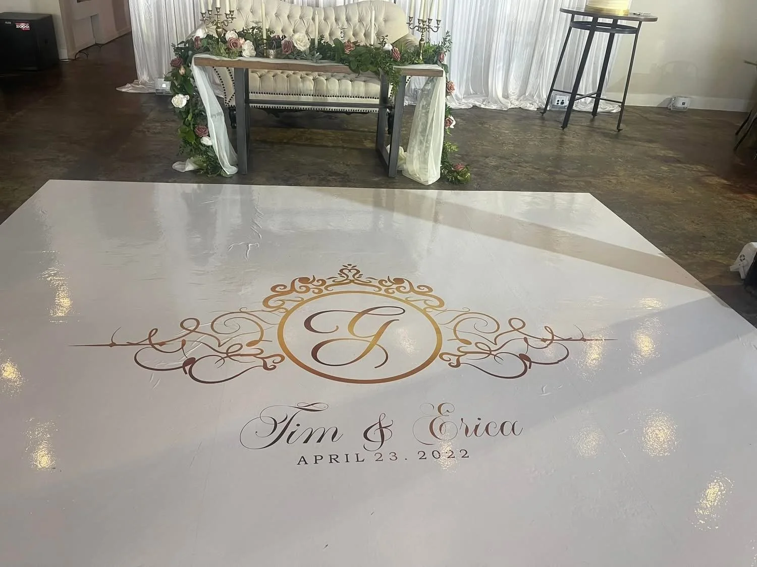 Wedding dance floor with initials 'T & E', wedding date April 23, 2022, and decorative designs, with a decorated sofa and floral arrangements in the background.