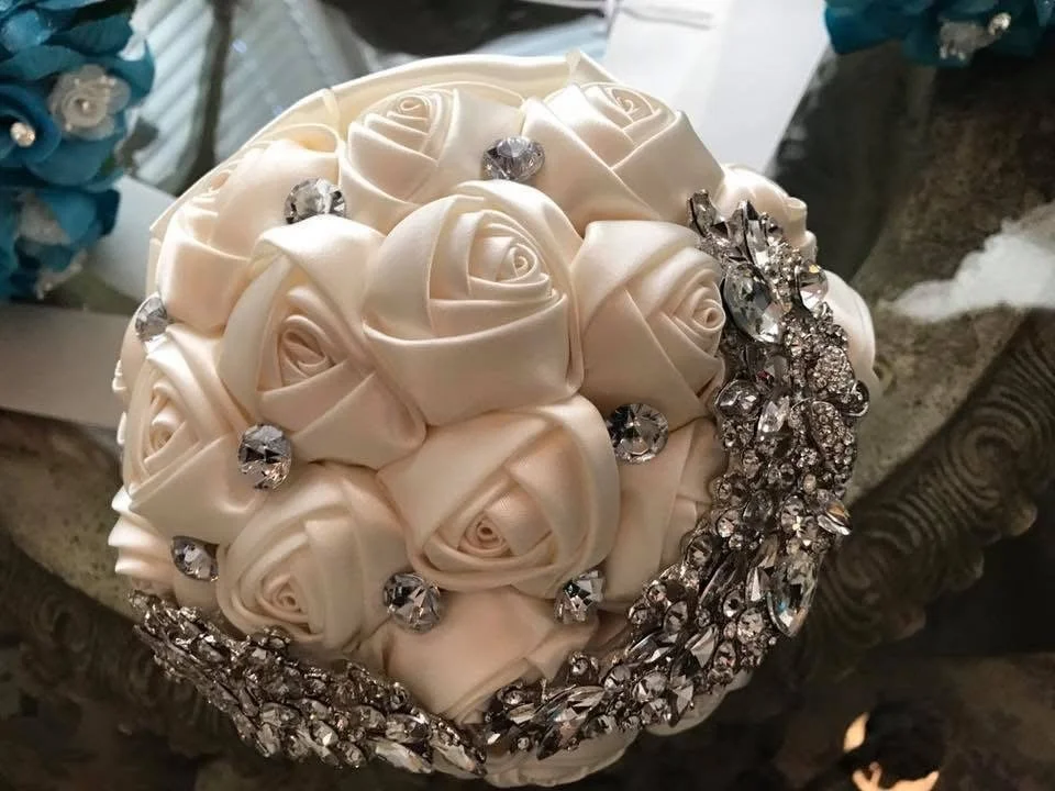 A decorative bouquet of white satin roses adorned with rhinestones and surrounded by sparkling crystal embellishments.