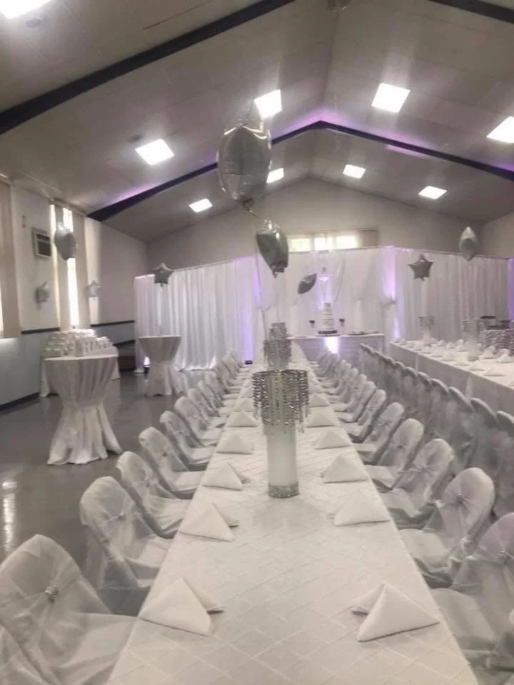 Decorated banquet hall with long white table, white chairs, and silver balloons