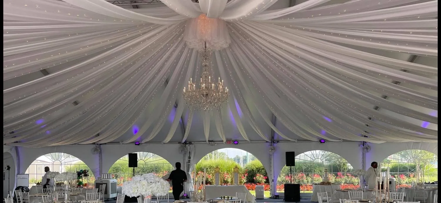Elegant event tent with white draped ceiling, crystal chandelier, and decorated tables inside
